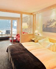Gemütliches Hotelzimmer mit Doppelbett, Bergbild an der Wand und Fensterblick auf verschneite Berge.