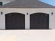 Double garage doors with dark wood finish on a white brick building, under a shingled roof.