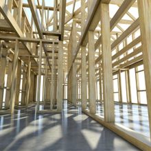 Wooden frame of a building under construction with sunlight casting shadows on the floor.