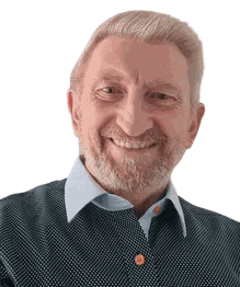 Ein lächelnder Mann mit Bart in einem gepunkteten Hemd und hellem Hintergrund.