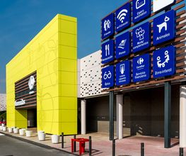 Edificio comercial amarillo con signos azules de servicios y accesos, como WiFi y zona infantil.