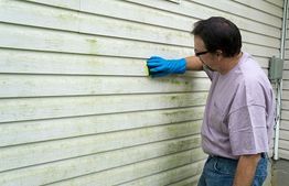 Man cleaning house siding with a sponge while wearing blue gloves.