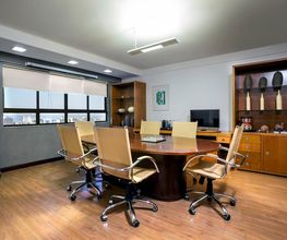 Sala de reuniões elegante com mesa oval, cadeiras estofadas e estante ao fundo.