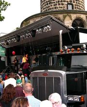 LKW-Bühne mit einer Band, die vor einer großen Menschenmenge bei einem Freiluftkonzert spielt.