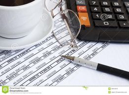 Xícara de café, óculos, caneta e calculadora sobre planilha com números.