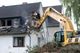 Excavator demolishing a house, breaking through the roof and walls.