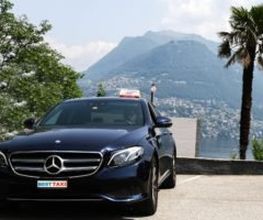 Schwarzes Taxi an malerischem Ort mit Bergen, Palmen und Natur im Hintergrund.