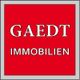 Rotes Logo mit weißem Text: "GAEDT IMMOBILIEN" in einem grauen Rahmen.