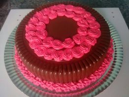 Bolo com cobertura de chocolate e decoração de chantilly rosa em espiral, sobre prato de vidro.