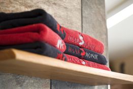 Rote und schwarze Handtücher gestapelt auf einem Holzregal in einem Badezimmer.