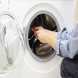 Hands fixing a washing machine by its open door.