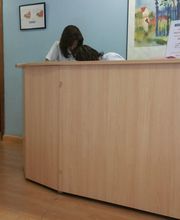 Recepción de una clínica con persona atendiendo detrás del mostrador de madera, personas esperando.