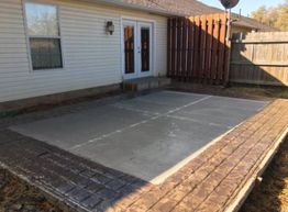 Concrete patio with brick border adjacent to a house and fenced yard.