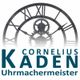 Schwarze Skelettuhr mit Zahnrädern und römischen Ziffern, Text: "Cornelius Kaden Uhrmachermeister".