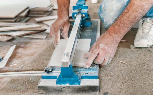 Ein Fliesenschneidearbeiter, der daran arbeitet Bodenfliesen passend zu zuschneiden.