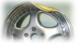 Verbogene silberne Felge mit sichtbarer Beschädigung am Rand vor unscharfem Hintergrund.