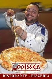 Persona felice serve una pizza, davanti all'insegna del ristorante "Odissea".