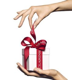 Deux mains tiennent un cadeau blanc avec un ruban rouge.