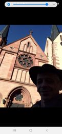 Eine Person mit Hut vor einer großen, alten Kirche mit zwei Türmen und einem runden Fenster.