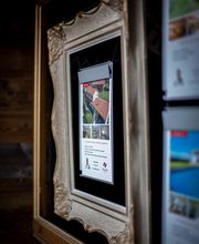 Bildschirm in einem goldenen Rahmen, zeigt Immobilien mit rotem Dach in einem Innenraum.