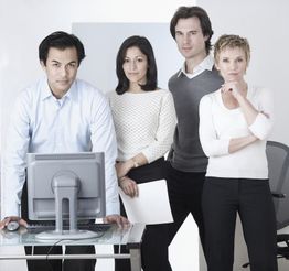 Vier Personen stehen um einen Tisch mit einem Computerbildschirm, freundlich und professionell.