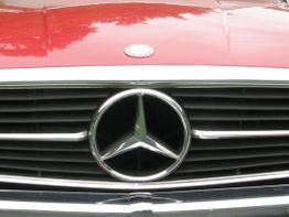 Nahaufnahme des Kühlergrills eines klassischen Autos mit rotem Lack und einem Mercedes-Logo.