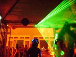 Festa com iluminação verde, luzes coloridas e convidados dançando no ambiente escuro.