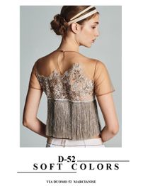 Modella di profilo con top trasparente e ricami, capelli raccolti, sfondo grigio. Scritta: D-52.