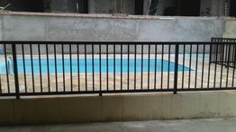 Piscina cercada por grade preta, situada em frente a uma parede de cimento.