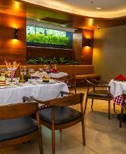 Restaurante elegante con mesas decoradas y luz cálida. Ventanas con plantas al fondo.
