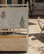 Cartel en terraza de café con ilustraciones botánicas y bicicletas, mesas y sillas alrededor.