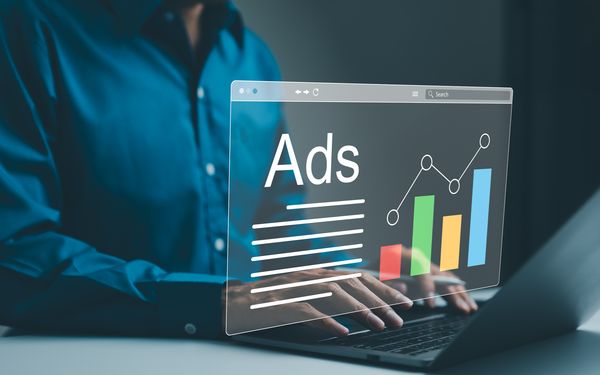 Eine Person tippt auf der Tastatur ihres Laptops. Eine Google-Ads-Grafik schwebt über der Tastatur. Darauf zu sehen ist ein Säulendiagram.