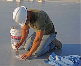 Worker kneeling on a surface, using a brush with a white bucket and blue cloth nearby.