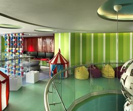 Área de juegos infantil con toldos de circo, pufs y decoración colorida en un espacio moderno.