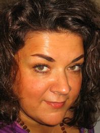 Eine Frau mit lockigem, dunklem Haar schaut direkt in die Kamera.