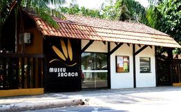 Fachada do Museu Sacaca, com telhado de telhas e vegetação ao fundo.