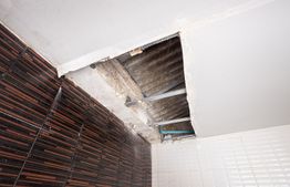 Hole in a tiled ceiling exposing pipes and insulation materials.
