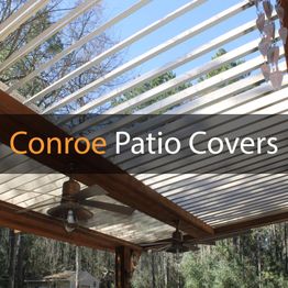 Louvered patio cover with ceiling fans and hanging decor against a blue sky and trees.