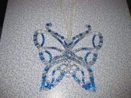 Schmetterlingsförmiger Schmuck mit blauen und weißen Perlen auf einem gemusterten Hintergrund.