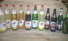 Zehn Flaschen verschiedener Getränke mit Etiketten, auf einem Holzuntergrund stehend.