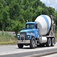 Blue cement mixer truck on a highway, surrounded by greenery.