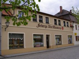 Zweistöckiges Gebäude mit der Aufschrift "Herberge Alte Meisterey" und Bäumen im Vordergrund.