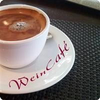 Tasse Kaffee auf einem Unterteller mit der Aufschrift "WeinCafé", auf einer dunklen Tischdecke.