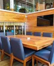 Sala de reuniones con mesa de madera, sillas azules, televisor y planta decorativa.