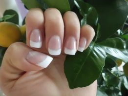 Eine Hand mit French Manicure vor grünen Blättern im Hintergrund.