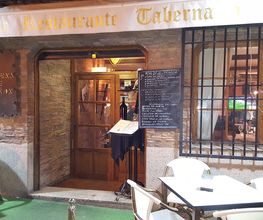 Entrada de una taberna con mesas al aire libre, menú en pizarra y decoración rústica.