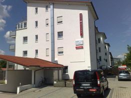 Weiße, mehrstöckige Wohngebäude mit parkenden Autos davor an einem sonnigen Tag.