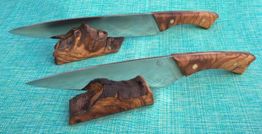 Zwei Messer auf Holzständern vor türkisem Hintergrund.