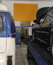 Dois carros em uma oficina, uma van azul e branca e um carro preto em uma plataforma elevatória.