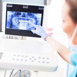 Dentist pointing at a dental X-ray on a screen with gloved hands.